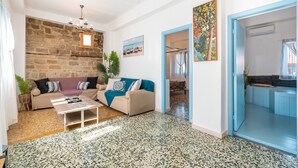 A living room with a stone wall, a sofa, a coffee table, and a door leading to a kitchen. - Holiday Home 'Katia's Home First Floor' with Shared Garden, Wi-Fi and Air Conditioning (Rhodes)