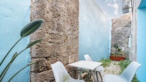 Un espacio exterior estrecho con un muro de piedra, un muro azul y una mesa con dos sillas.