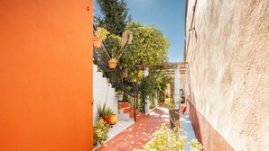 Un callejón estrecho con un sendero rojo, plantas en macetas y una estructura de pérgola.