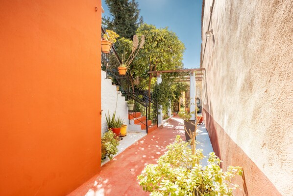 Une ruelle étroite avec un chemin rouge, des plantes en pot et une structure en forme de pergola.