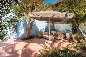 Un espace extérieur aménagé avec des sièges, un grand parasol, des meubles en osier et des plantes en pot.