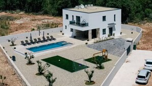 Un edificio moderno de dos pisos con piscina, cancha de tenis y zona de estacionamiento.