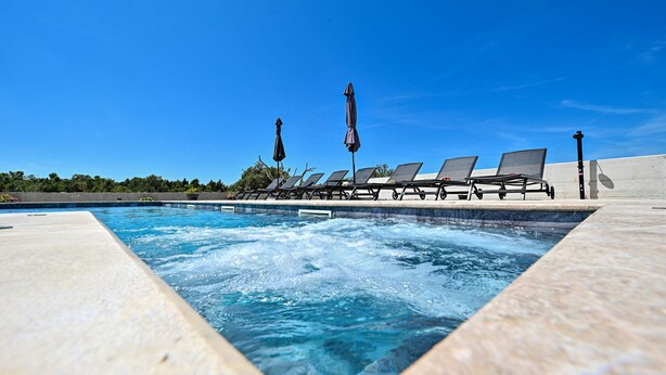 Una piscina con sillas de descanso y sombrillas, bajo un cielo azul y despejado.
