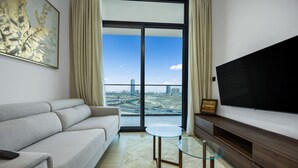 Een moderne woonkamer met een bank, een glazen salontafel, een flatscreen televisie en een uitzicht op een stadsbeeld door grote ramen.