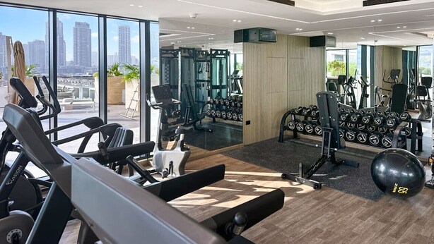 Een moderne sportschool met diverse fitnessapparaten, grote ramen met uitzicht op de stad en een overzichtelijke, nette indeling.