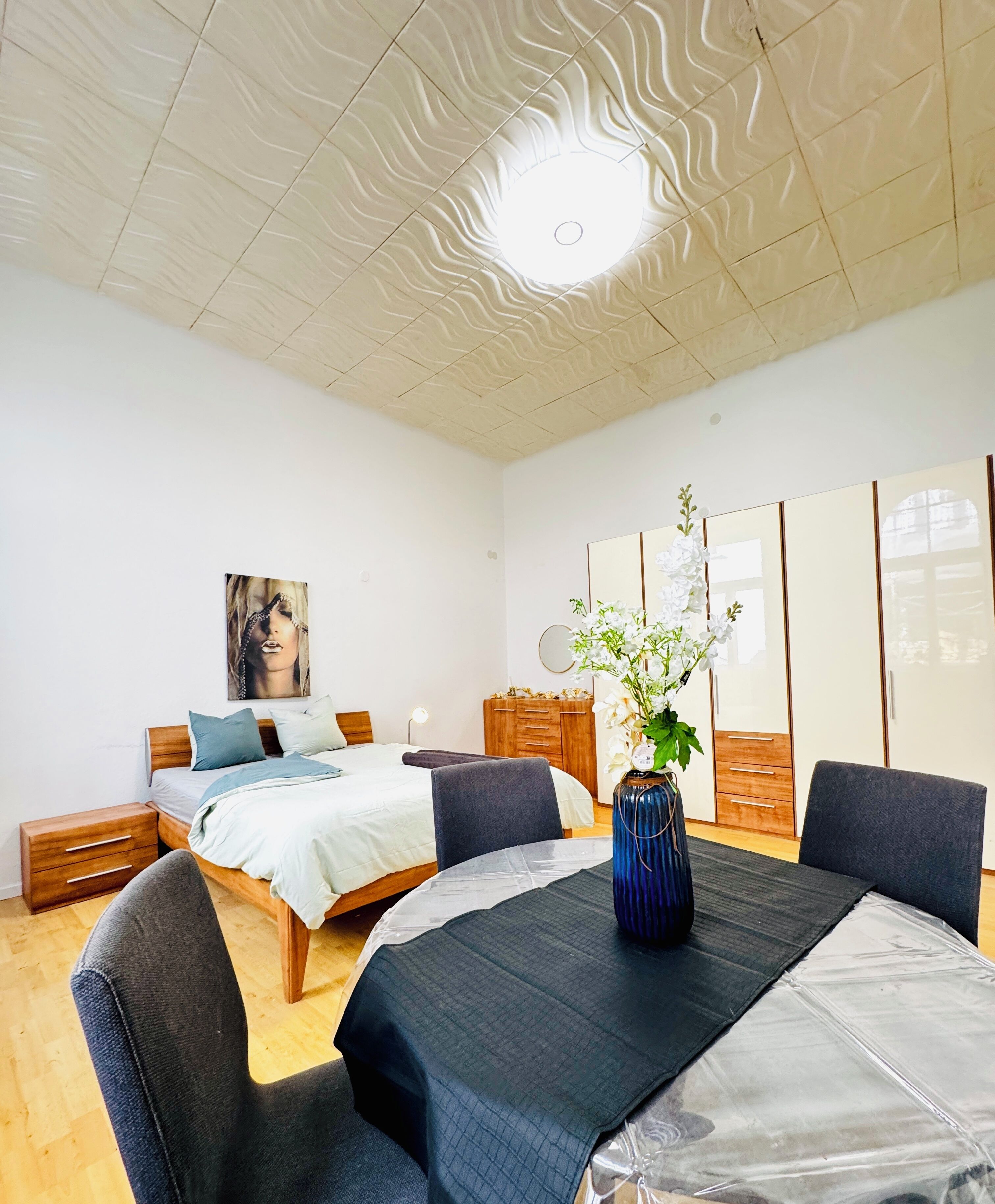 Quarto moderno com cama de madeira, mesa de cabeceira, cômoda e uma janela grande.