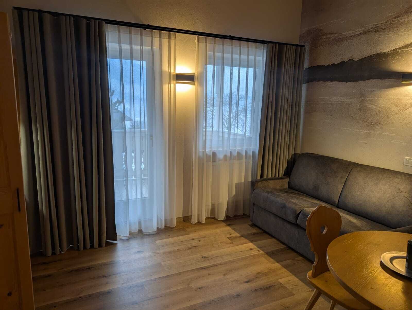 A cozy living room with a sofa, a wooden table, and sheer curtains.