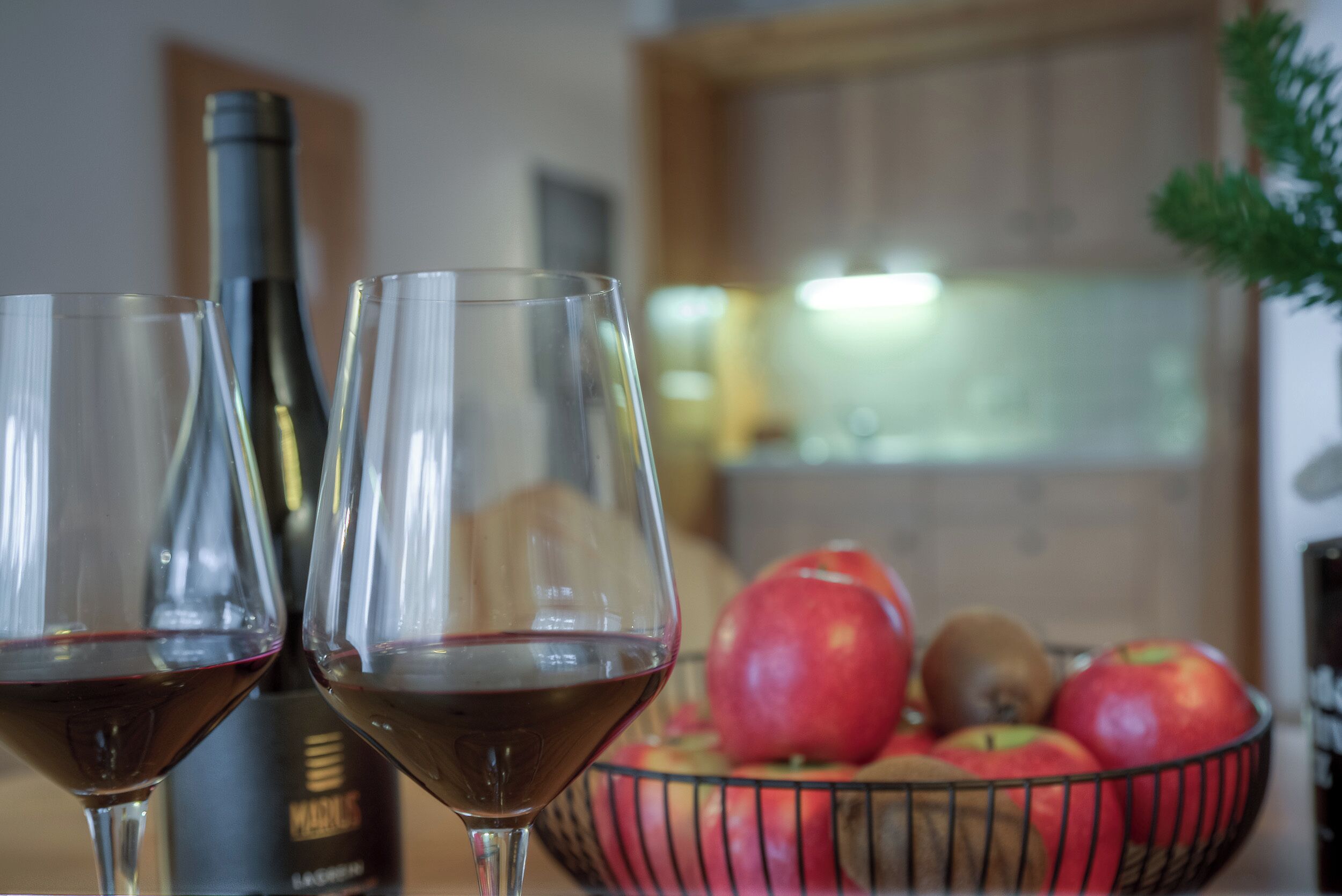 Dos copas de vino tinto, una botella y un cuenco con manzanas.