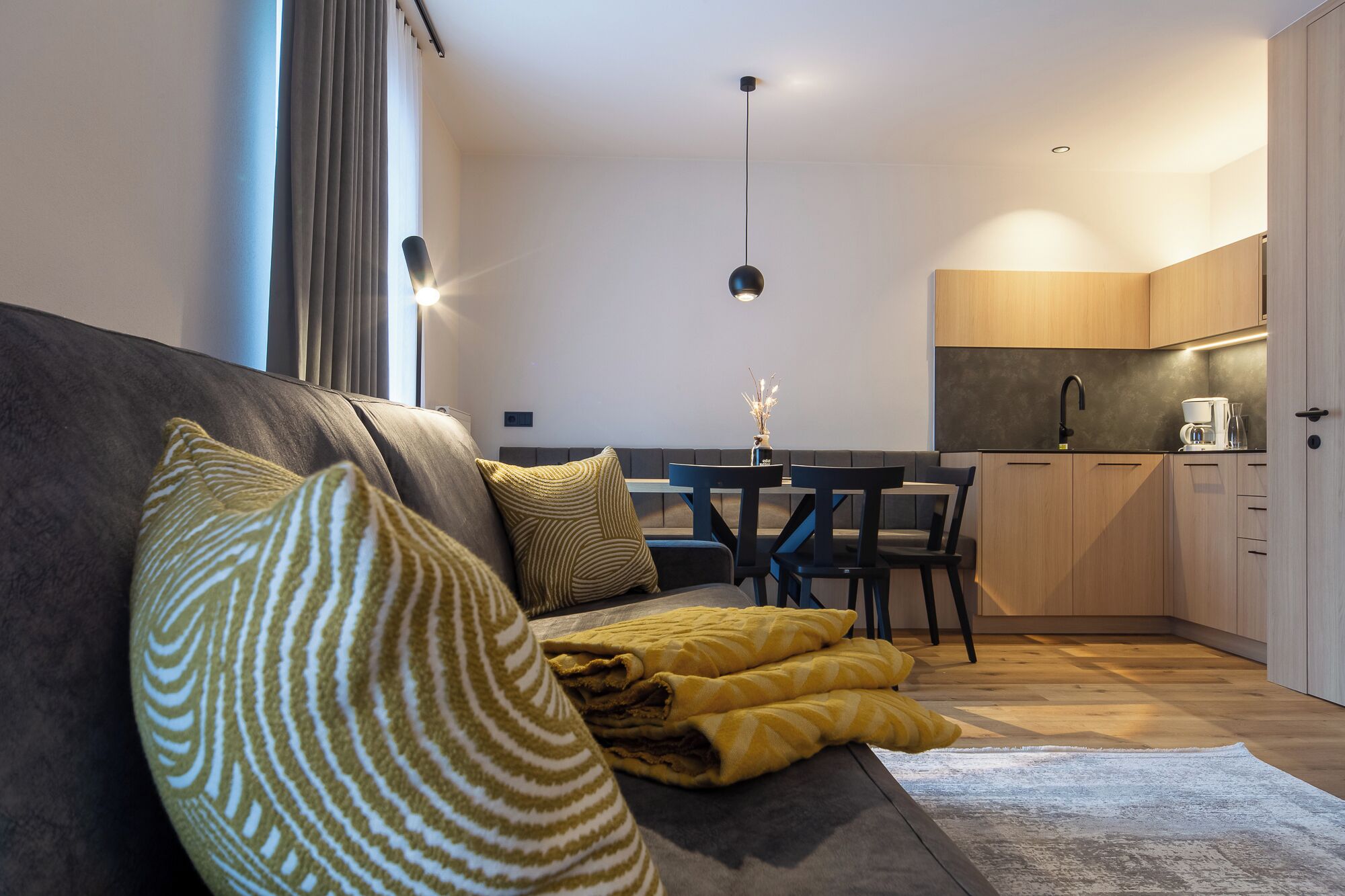 A modern living room with a sofa, a dining table, and a kitchen area.
