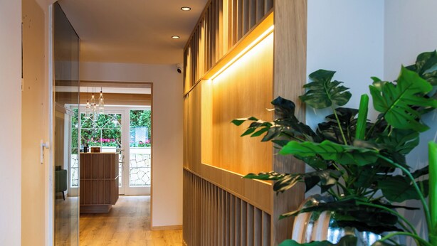 Un pasillo con un revestimiento de madera, una puerta de vidrio que da a una habitación y una planta en maceta.