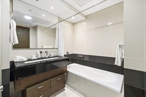 A modern bathroom with a black vanity, a large mirror, a white bathtub, and a shower area. - 2BR Partial Burj Khalifa View (Dubai)