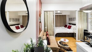 A hotel room with a large mirror, a bed with red and white bedding, a sofa with striped cushions, a small round table with a red and white patterned coaster, and a potted plant. - Cozy condo with AC in soothing near Rockwell (Mandaluyong City)