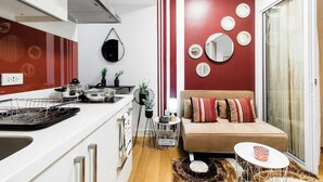A compact living space with a kitchenette, a sofa with striped cushions, a coffee table, and a wall with circular mirrors. - Cozy condo with AC in soothing near Rockwell (Mandaluyong City)