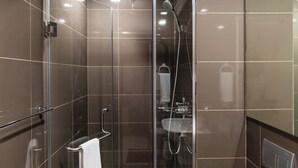 A modern bathroom with a glass-enclosed shower, a glass door, and a visible sink area. - Cozy condo with AC in soothing near Rockwell (Mandaluyong City)
