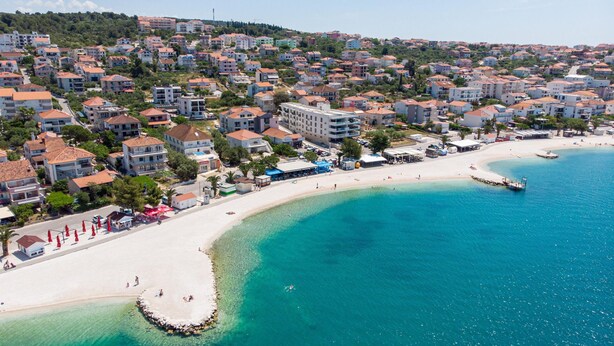 An aerial view of a coastal town with a sandy beach, clear blue waters, and residential buildings. - Beachfront apartment fully equipped with terrace and seaview, parking included. (Okrug Gornji)