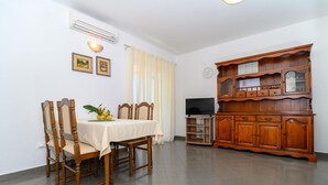 A dining area with a table set for four, wooden chairs, a cabinet with glass doors, and a television on a stand. - Beachfront apartment fully equipped with terrace and seaview, parking included. (Okrug Gornji)