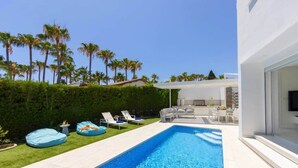 Un espace piscine extérieur moderne, doté de chaises longues, d’un barbecue et offrant une vue sur les palmiers.