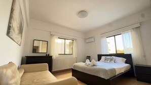 Een slaapkamer met een bed, een bank, een dressoir en een raam.
