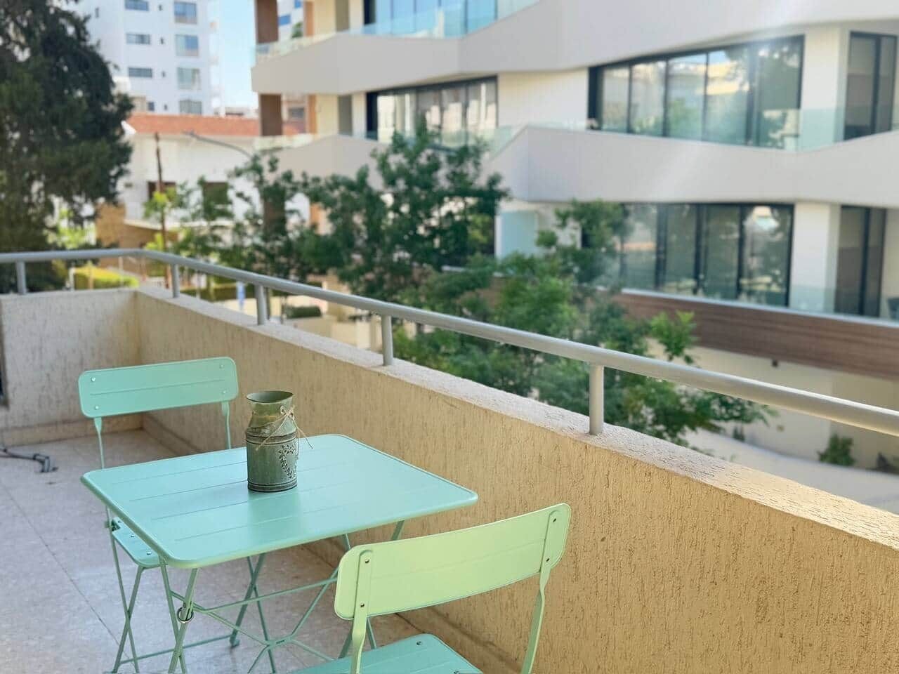 Un balcón con una mesa, sillas, un contenedor metálico y una barandilla.