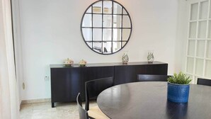 Een eetruimte met een ronde tafel, stoelen, een donkere kast en een decoratieve spiegel aan de muur.