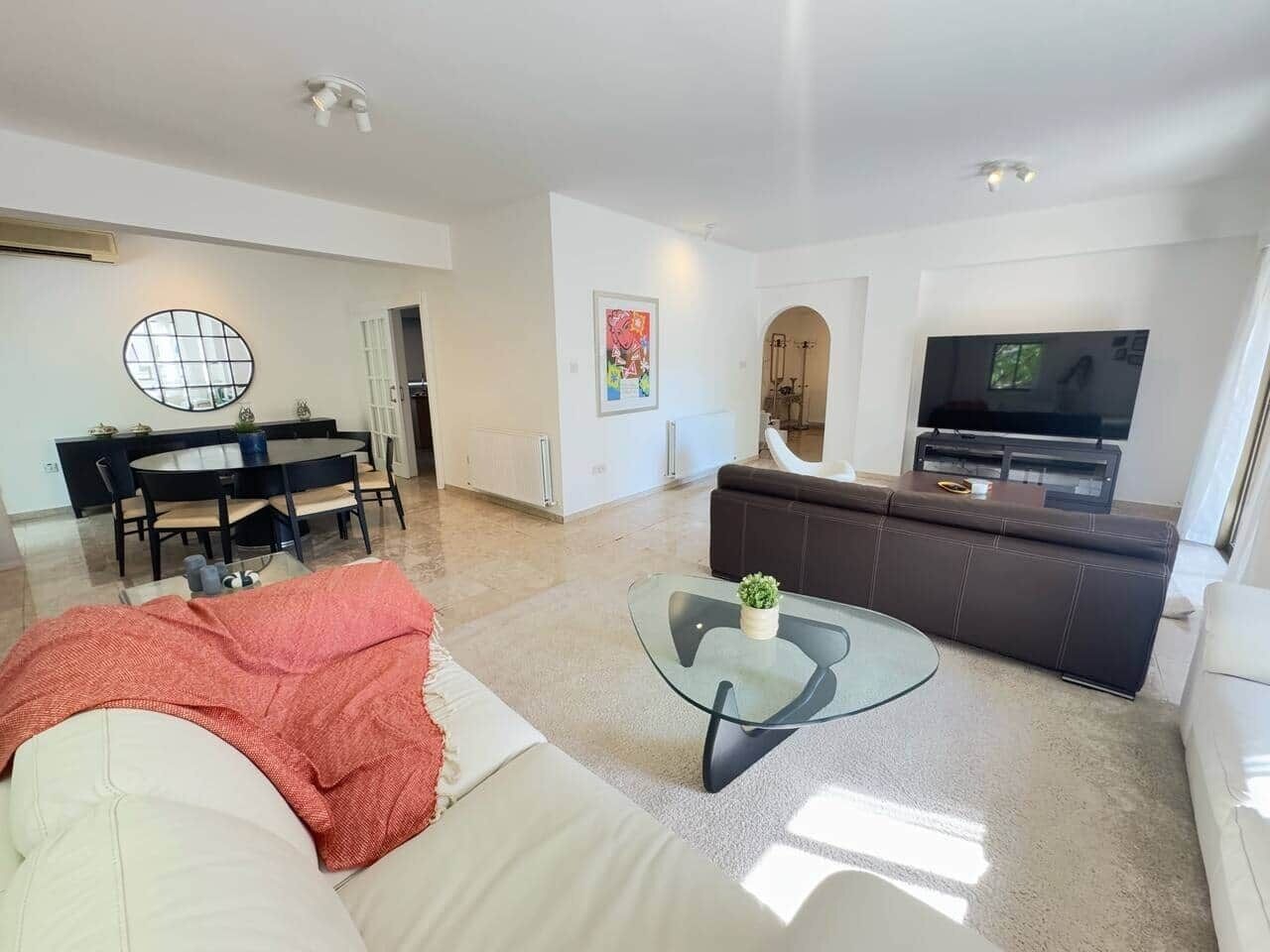 Una sala de estar moderna con una mesa de centro de vidrio, un sofá, una zona de comedor con una mesa redonda y un televisor.