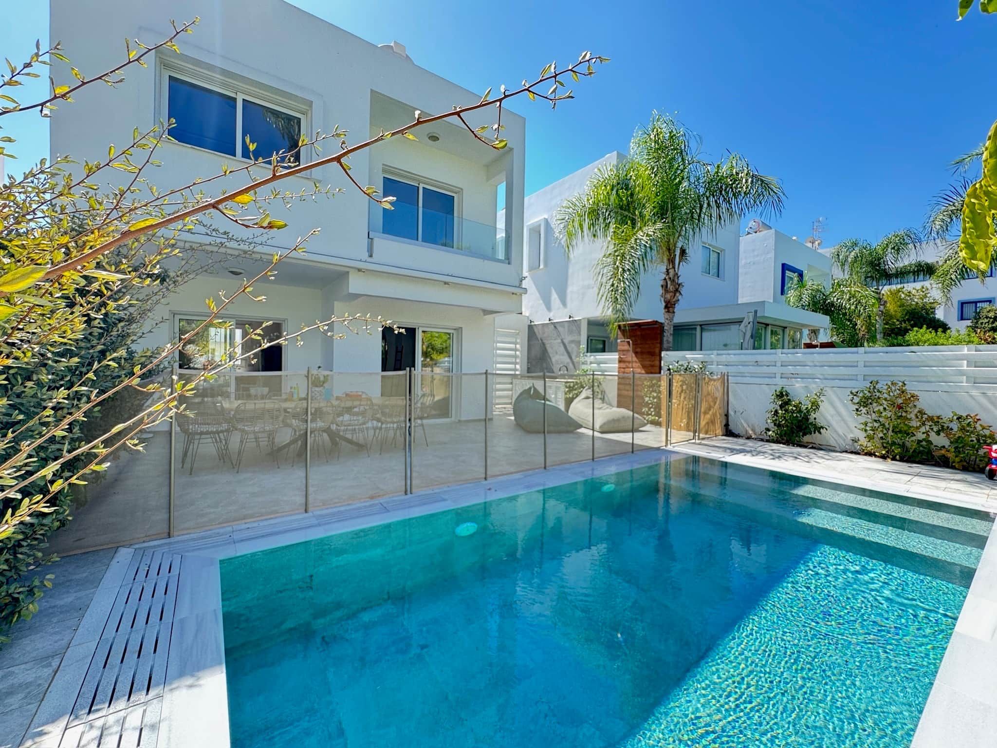 Une maison moderne à deux étages, dotée d’une piscine, d’un patio couvert et offrant une vue sur les maisons voisines.