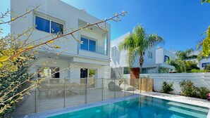 Uma casa moderna com dois andares, piscina, varanda coberta e vista para as casas vizinhas.