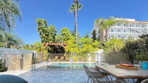 Área de piscina com pergolado, espreguiçadeiras e mesa de jantar com cadeiras.