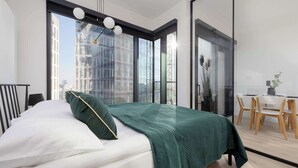 Ein modernes Hotelzimmer mit einem großen Bett, einem Essbereich und Blick auf die Stadt durch große Fenster.