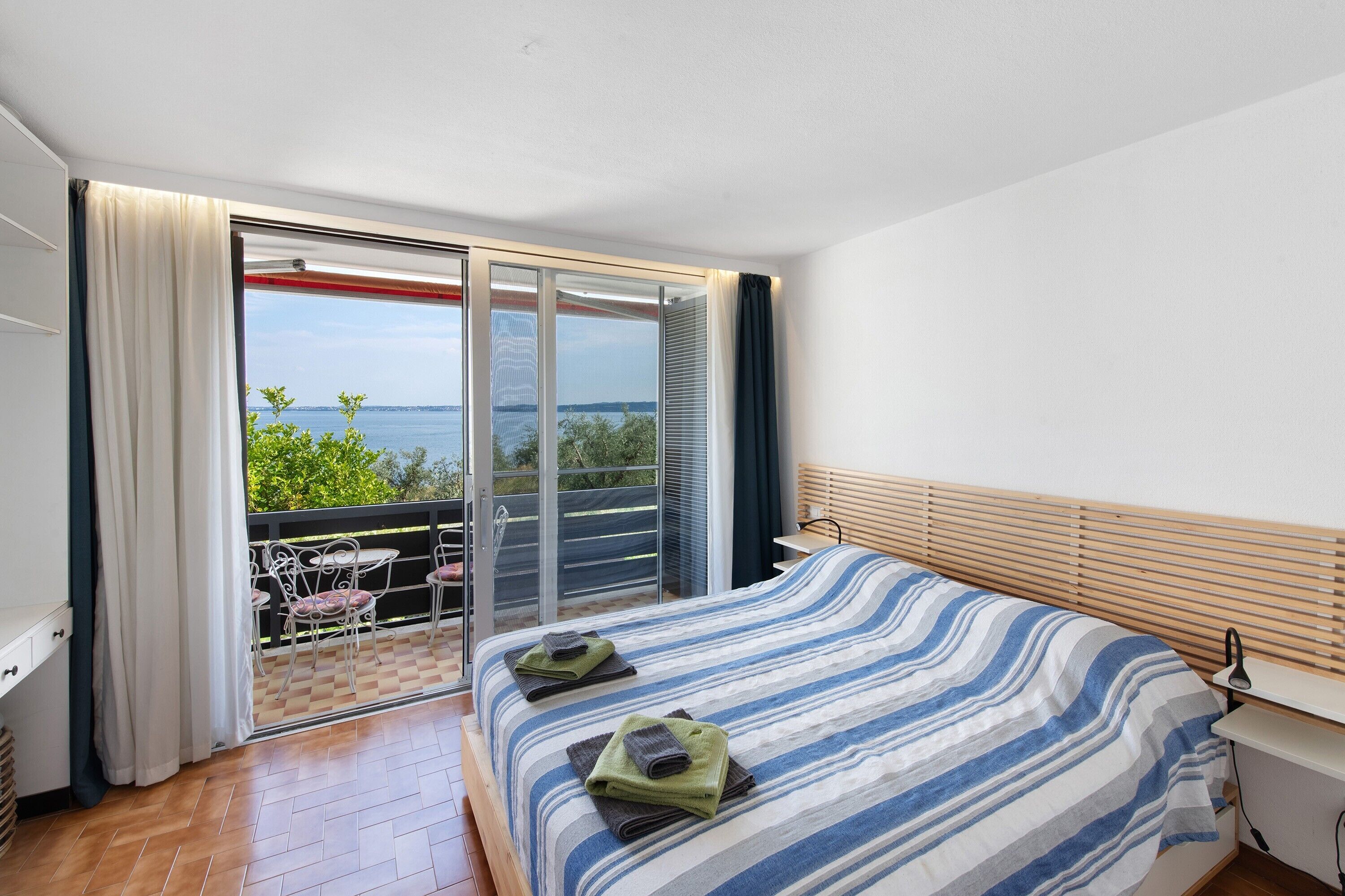Quarto com cama, vista para o mar, varanda com cadeiras e janela com cortinas.