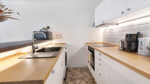 A compact kitchen with a sink, stove, and coffee maker, featuring white cabinets and a stone backsplash. - Holiday Home 'Casa Liner - Steps From The Lake' with Lake View, Private Terrace and Wi-Fi (Moniga del Garda)
