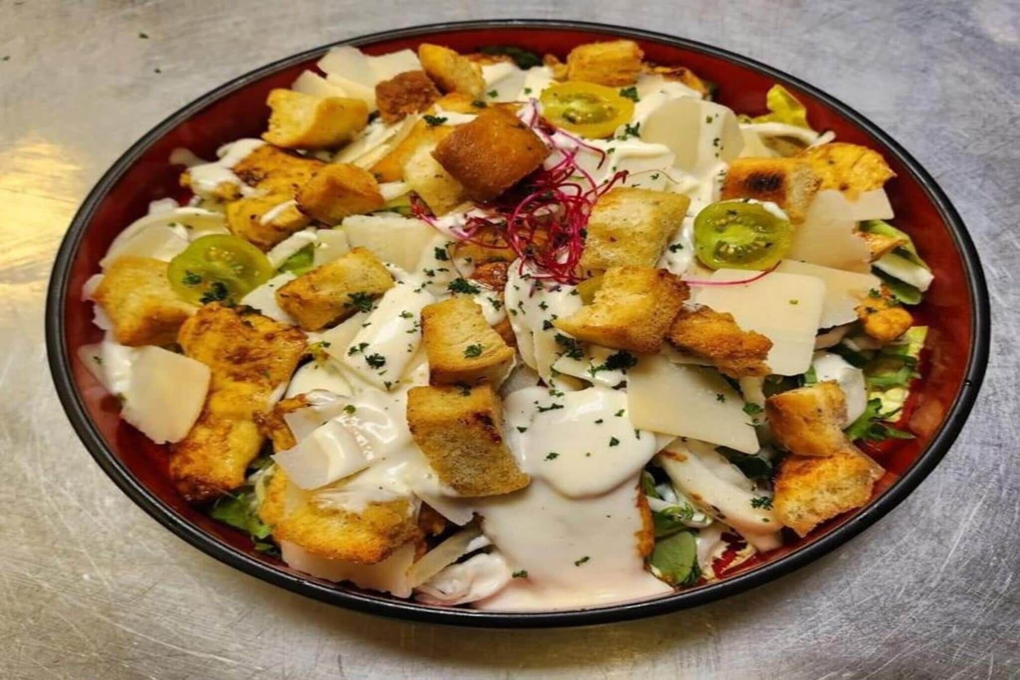 Een saladekom met croutons, kaas en een romige dressing.