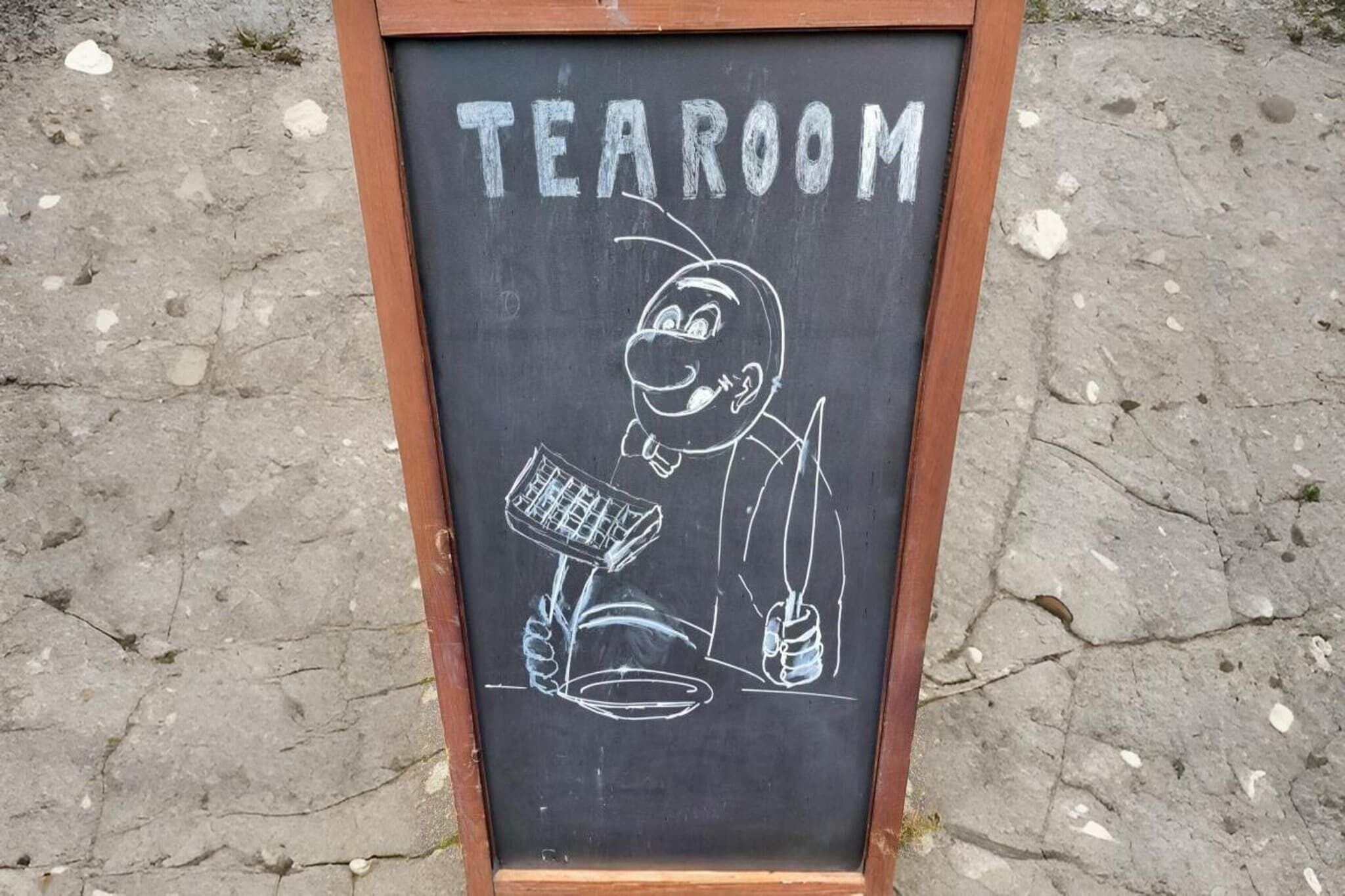 Un tableau noir sur lequel est écrit le mot « SALON DE THÉ » et est dessiné un personnage tenant un marteau et une plante.