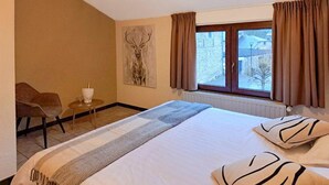 Une chambre d’hôtel avec un lit, une chaise, une petite table avec un verre et une fenêtre avec des rideaux.