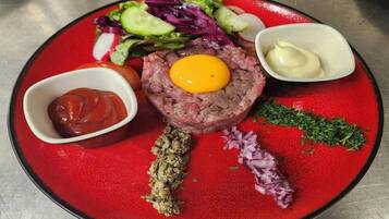 Ein Teller mit einem rohen Fleischgericht, belegt mit einem Eigelb, dazu ein gemischter Salat, Ketchup und eine kleine Schale Sauce.