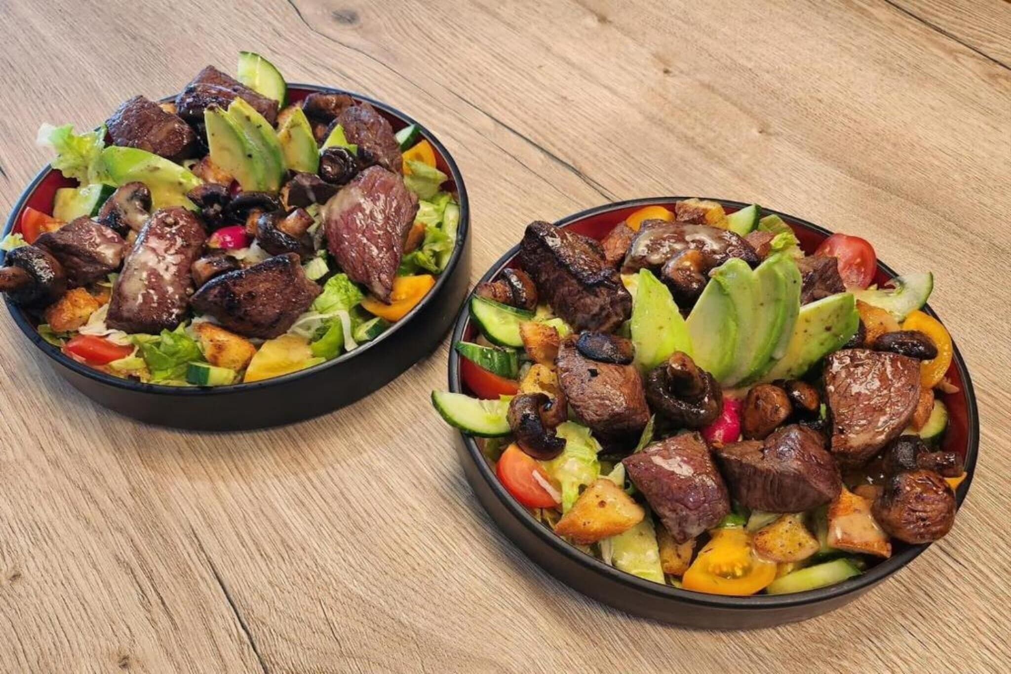 Deux salades composées de viande grillée, d’avocat et de légumes.