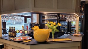 Un espace bar avec un comptoir, des bouteilles, des verres et un pichet jaune.