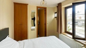 Habitación de hotel con cama, armario, espejo, ventana con vista a la calle y radiador.