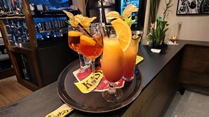 Una zona de bar con tres bebidas en una bandeja, una barra y una pared decorativa con un cuadro enmarcado.