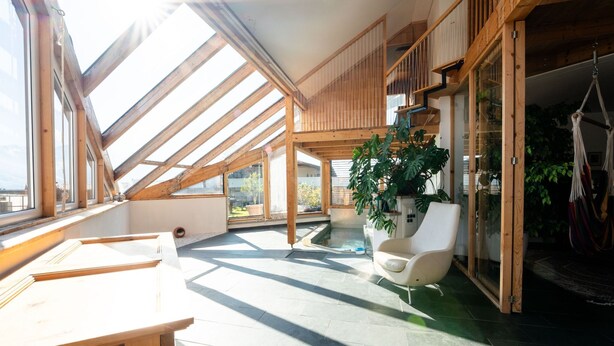 A spacious room with skylights, a potted plant, a white chair, and a wooden table. - Chalet Innerwald (Gnadenwald)