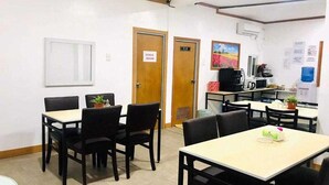 Un espace repas avec des tables et des chaises, un coin cuisine et un panneau indiquant l’emplacement du local de stockage.