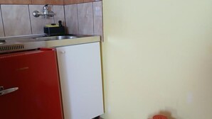 A compact kitchen with a sink, a red refrigerator, and a small trash bin.