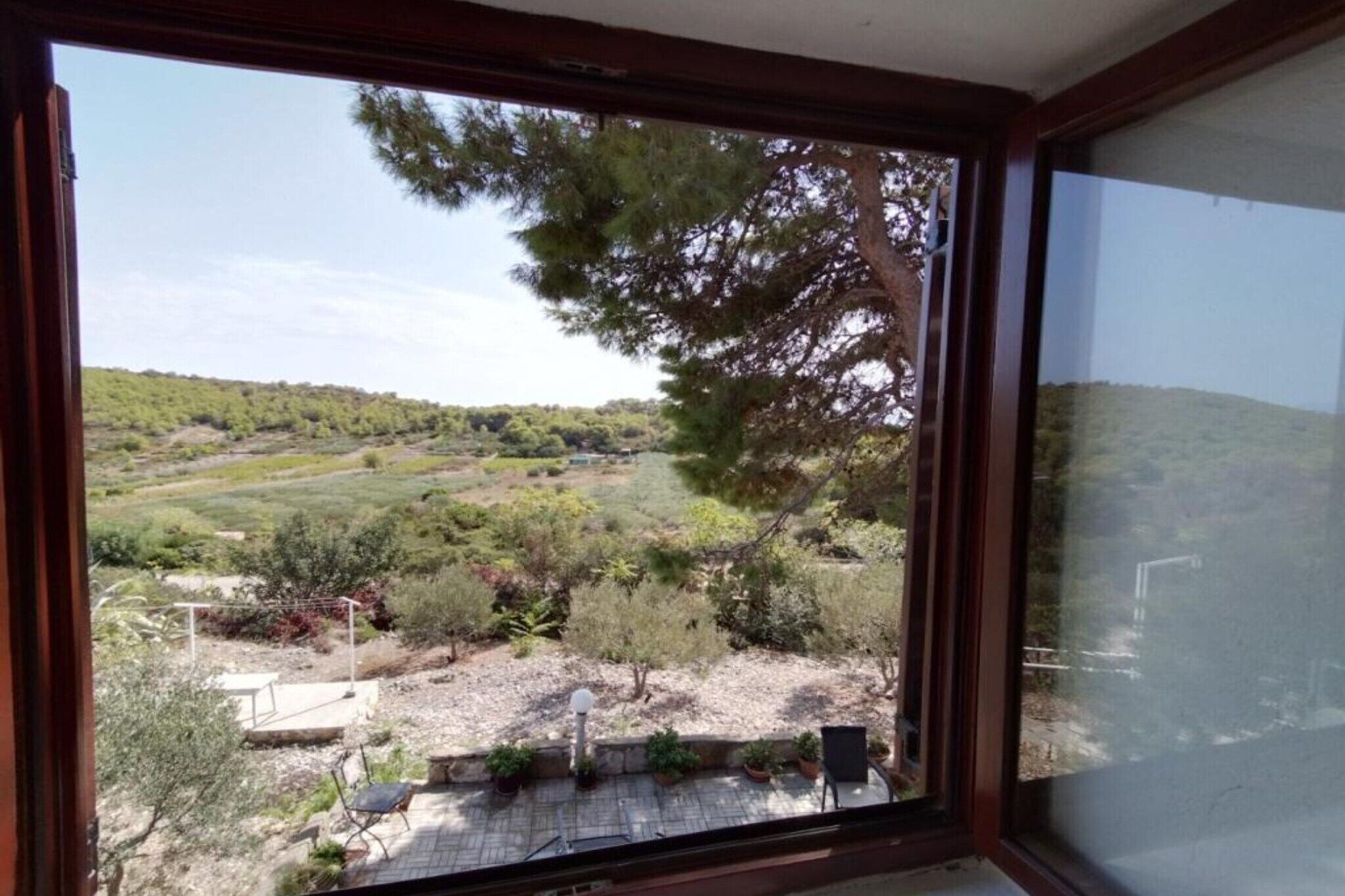 A room with a large window overlooking a landscaped garden with trees and shrubs.