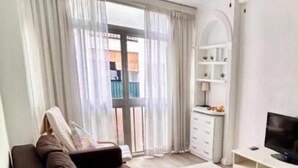 Een woonkamer met een bank, een televisie, een plafondventilator en uitzicht door een raam.
