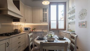 A modern kitchen with white cabinets, a gas stove, a microwave, and a dining table set for four. - Italianway Easy - Rosales 3 C (Milan)
