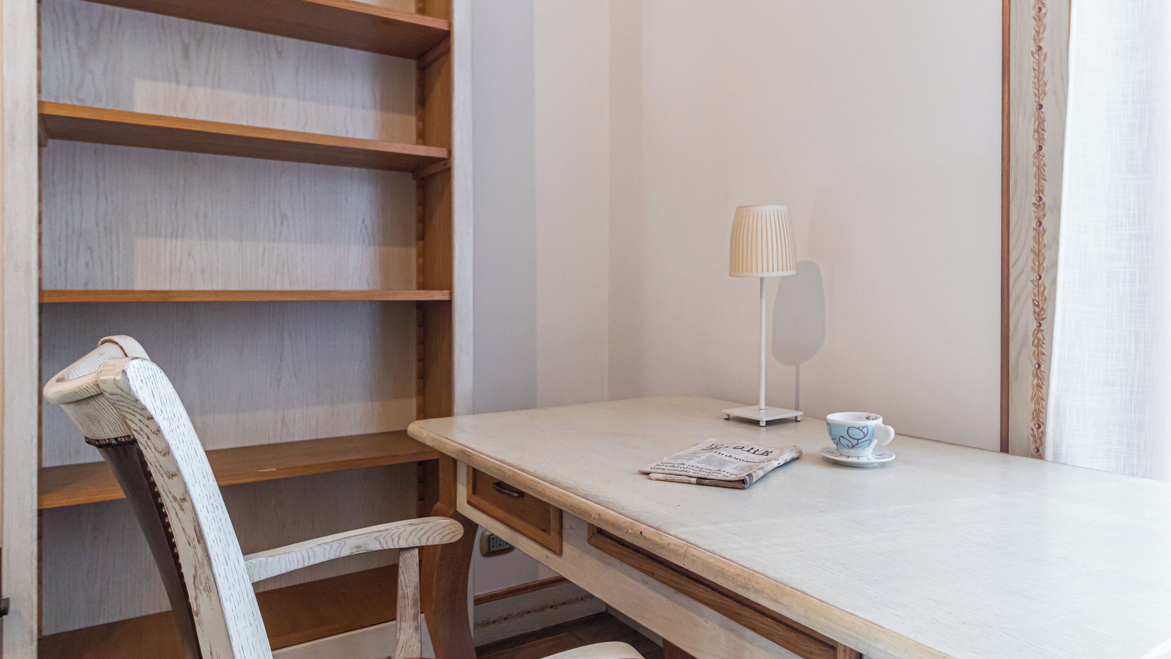 A small, neatly organized workspace with a wooden chair, a white desk, a lamp, and a cup.