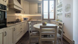 A kitchen with white cabinets, a stove, a microwave, and a dining table with chairs. - Italianway Easy - Rosales 3 C (Milan)