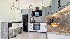 A modern kitchen with grey cabinets, a central island with bar stools, a built-in oven, and a fruit bowl on the counter. - Villa Aglaia in Mparmpati (Corfu)