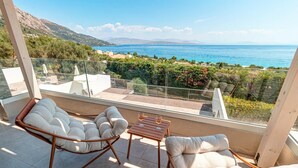 A balcony with two cushioned chairs and a small table, overlooking a coastal landscape with a clear view of the sea and distant mountains. - Villa Aglaia in Mparmpati (Corfu)