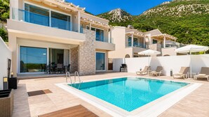 A modern pool area with a clear blue pool, lounge chairs, and a mountain backdrop. - Villa Aglaia in Mparmpati (Corfu)